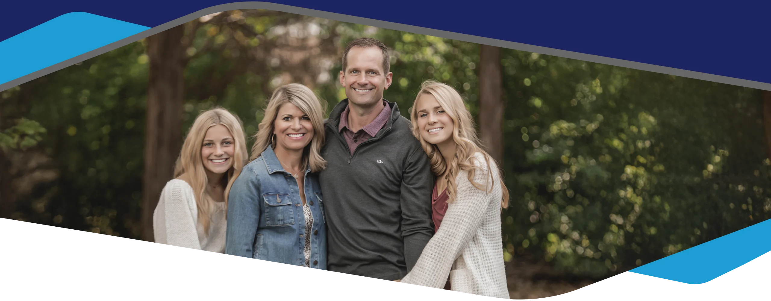 Dr. Adam Williams and family standing outdoors with trees in the background, dressed in casual fall clothing and posing closely together.